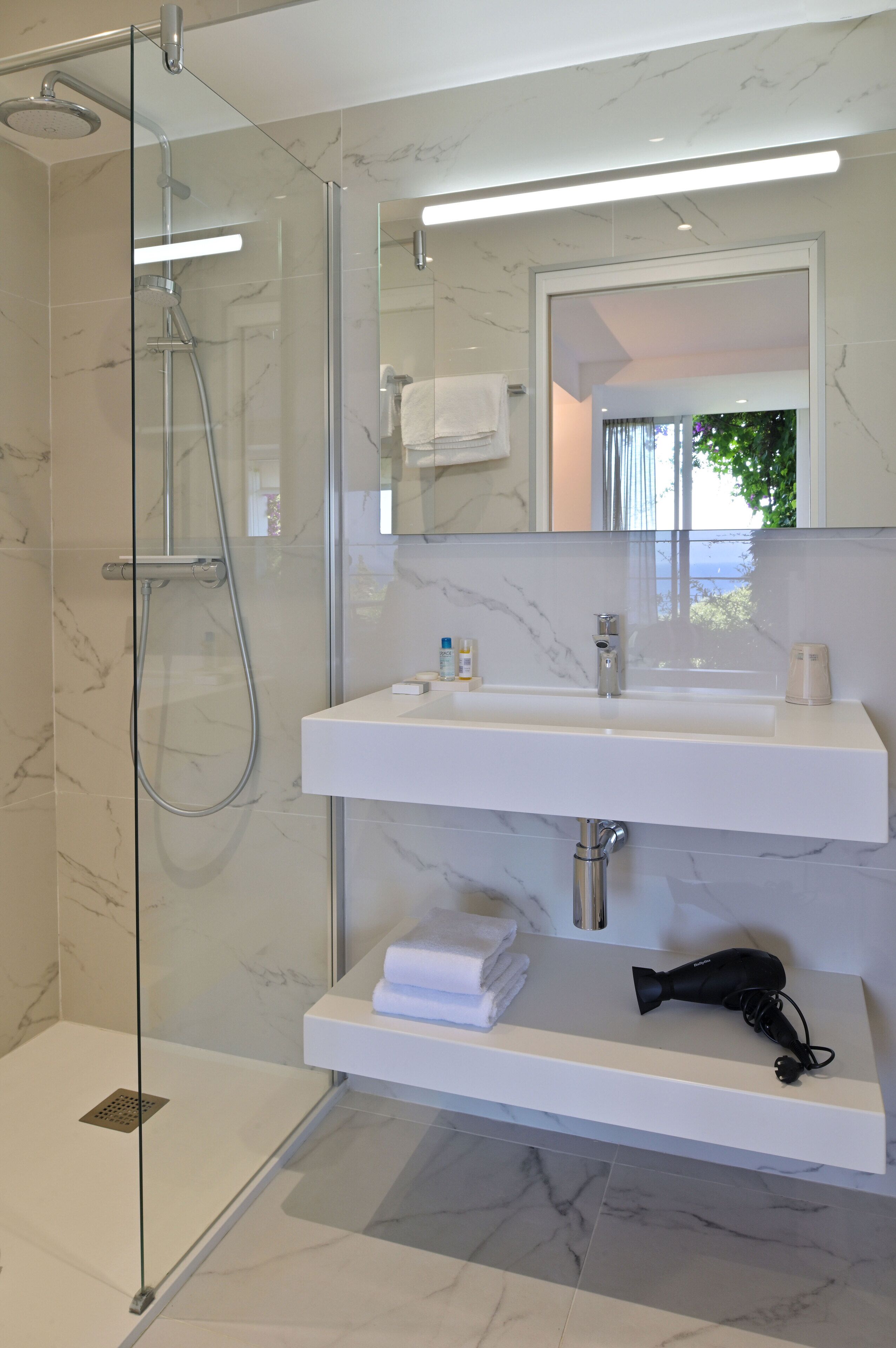 A modern bathroom with a glass-enclosed shower, a white sink with a mirror above it, and a hairdryer on the sink's edge.