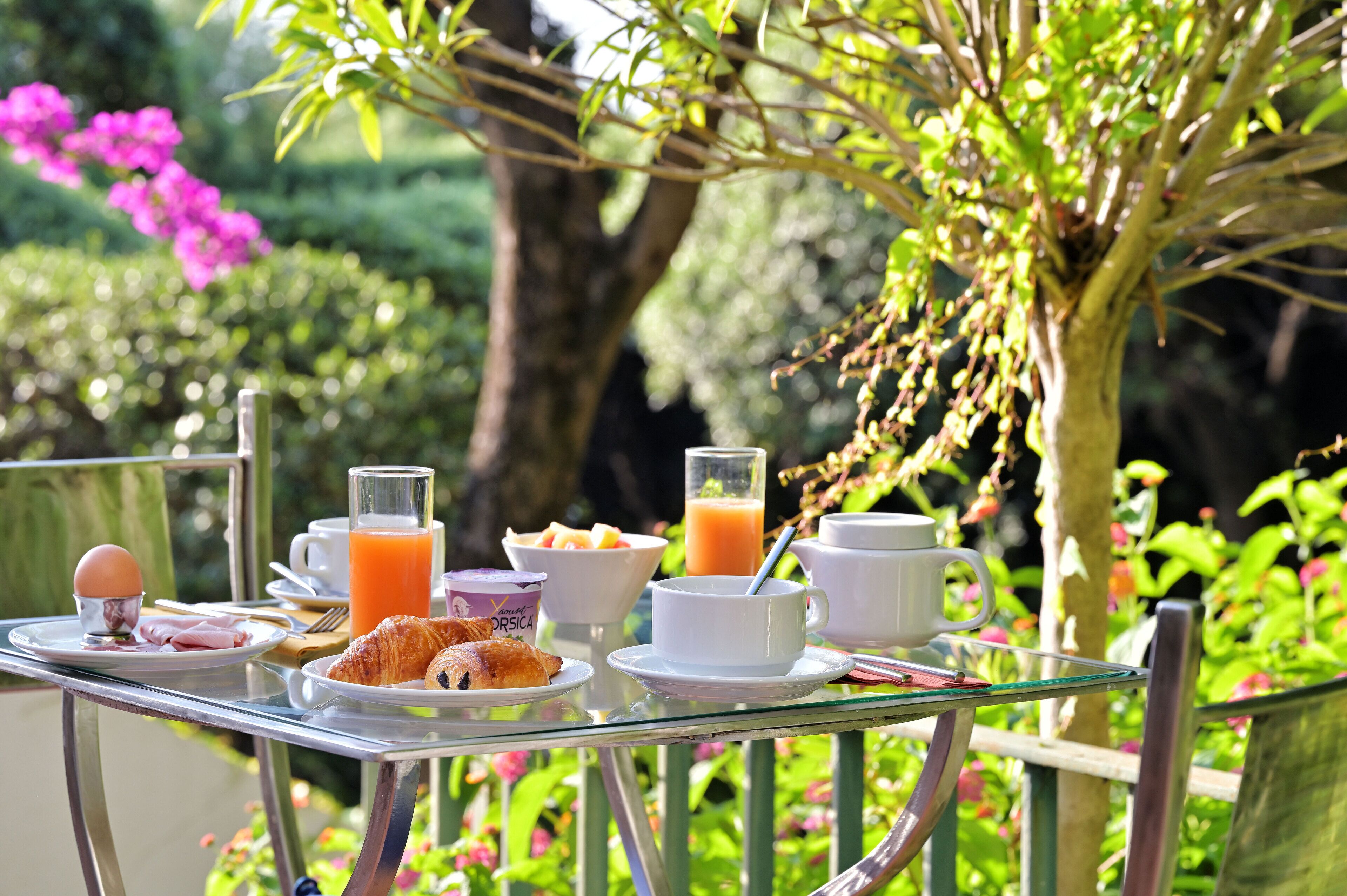A breakfast table set outdoors with plates of food, cups, and a glass of orange juice.