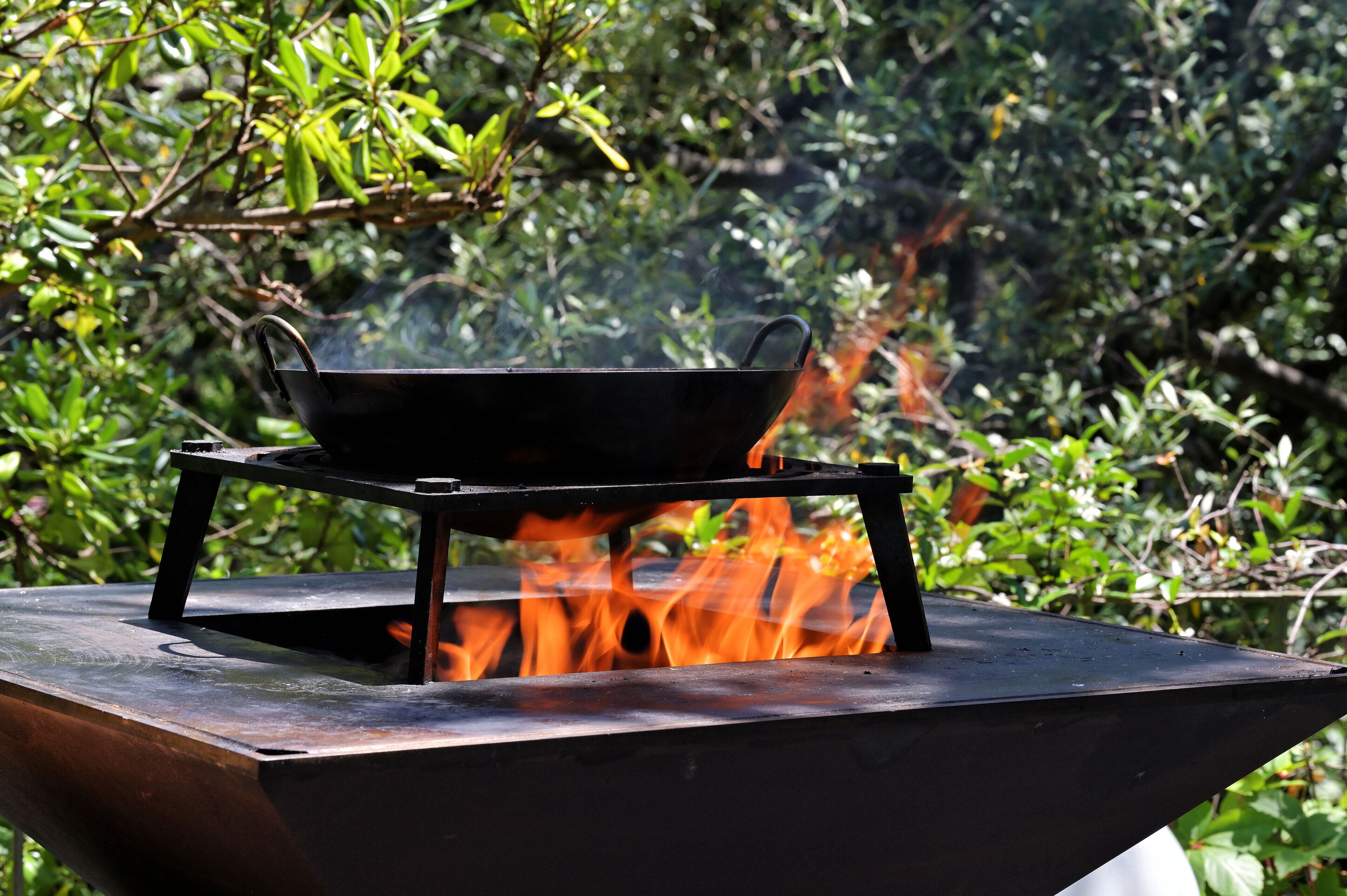 Estufa de camping portátil con un wok encima, rodeado de llamas, sobre un soporte de metal.