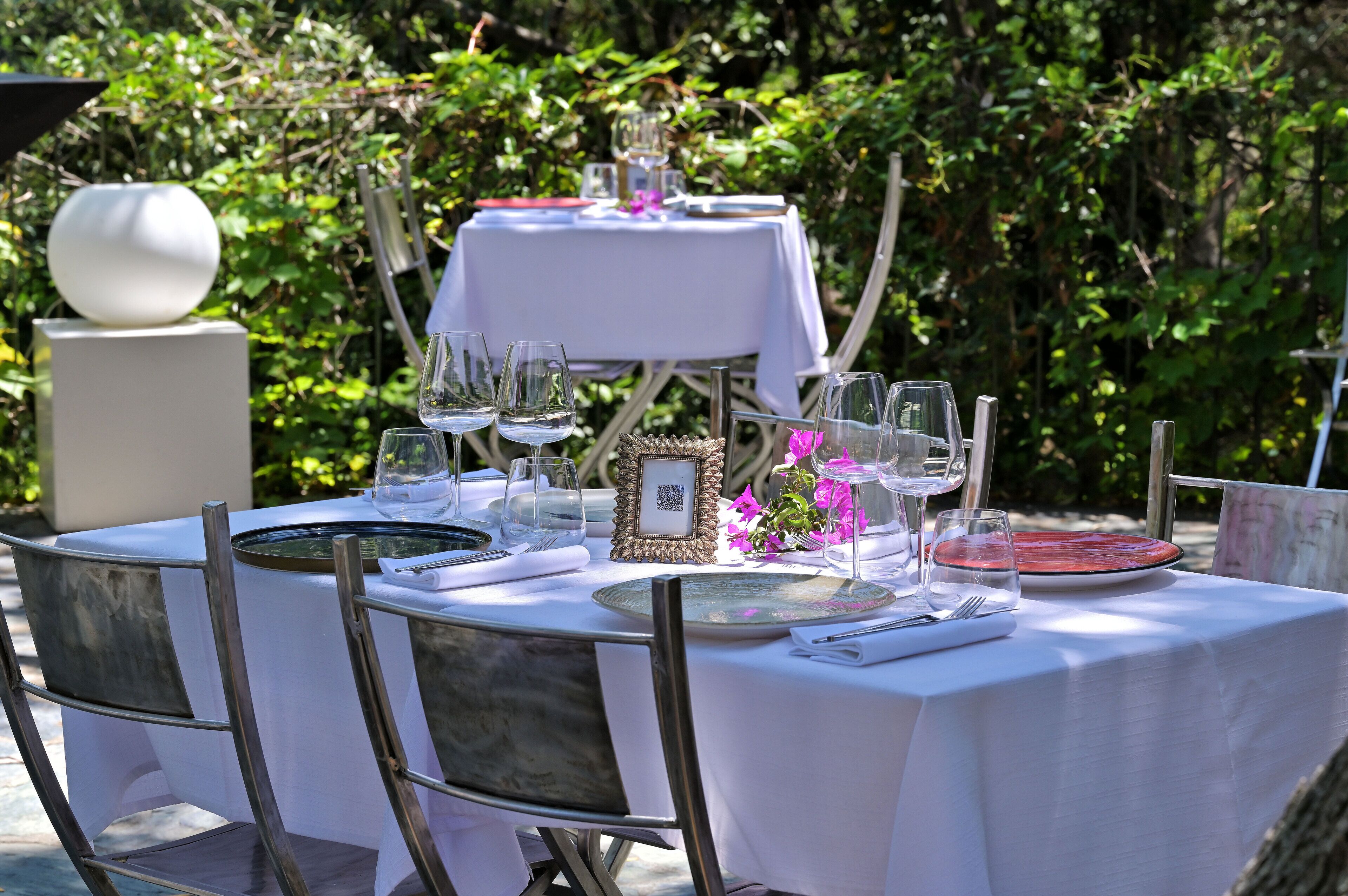 An outdoor dining table set with white tablecloth, multiple wine glasses, plates, and cutlery.