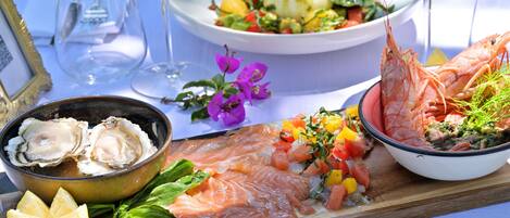 A seafood platter with various dishes including salmon, shrimp, and oysters, accompanied by drinks and a salad.