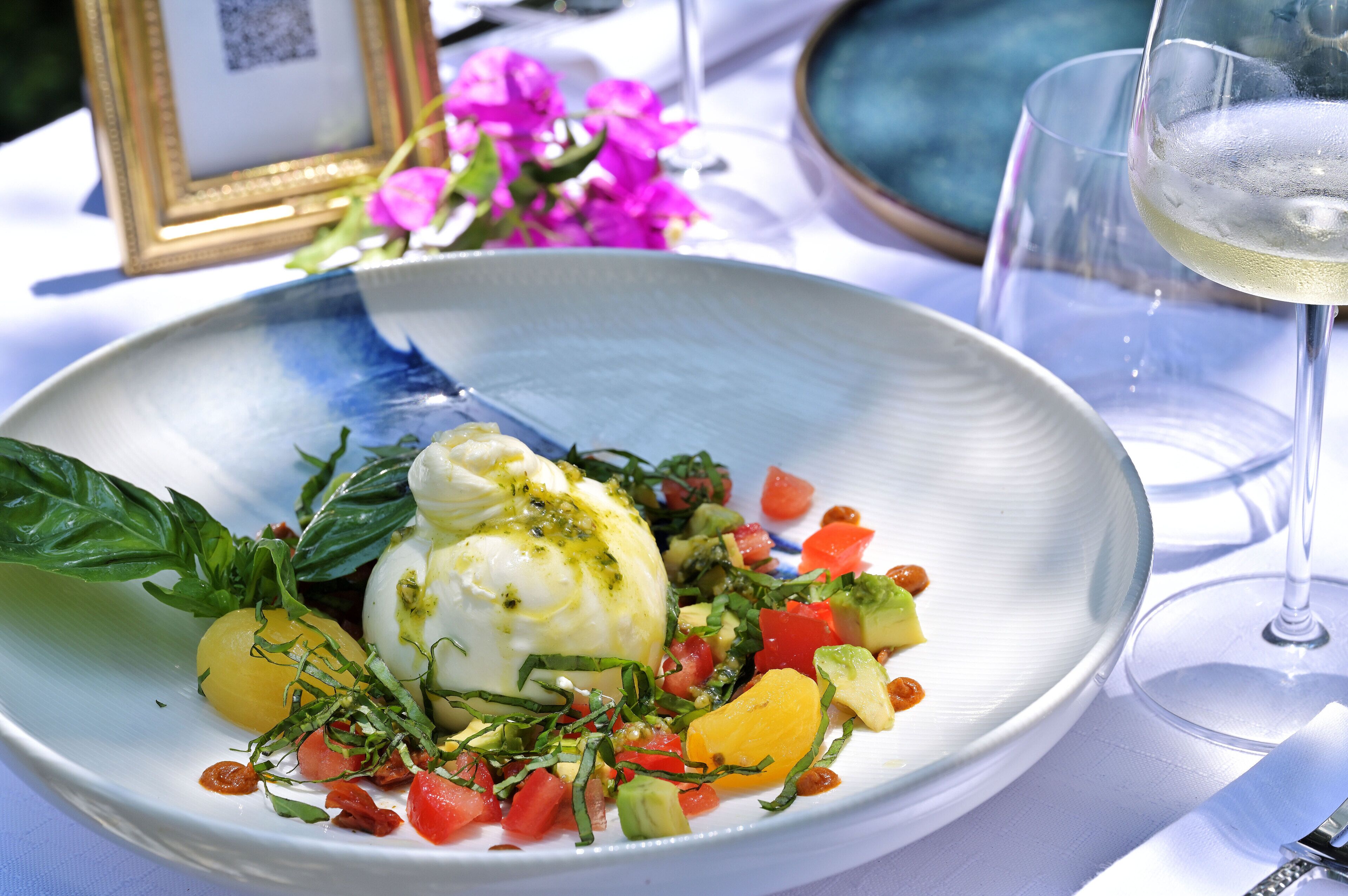 Un plato de comida con salsa blanca, verduras y una copa de vino blanco.