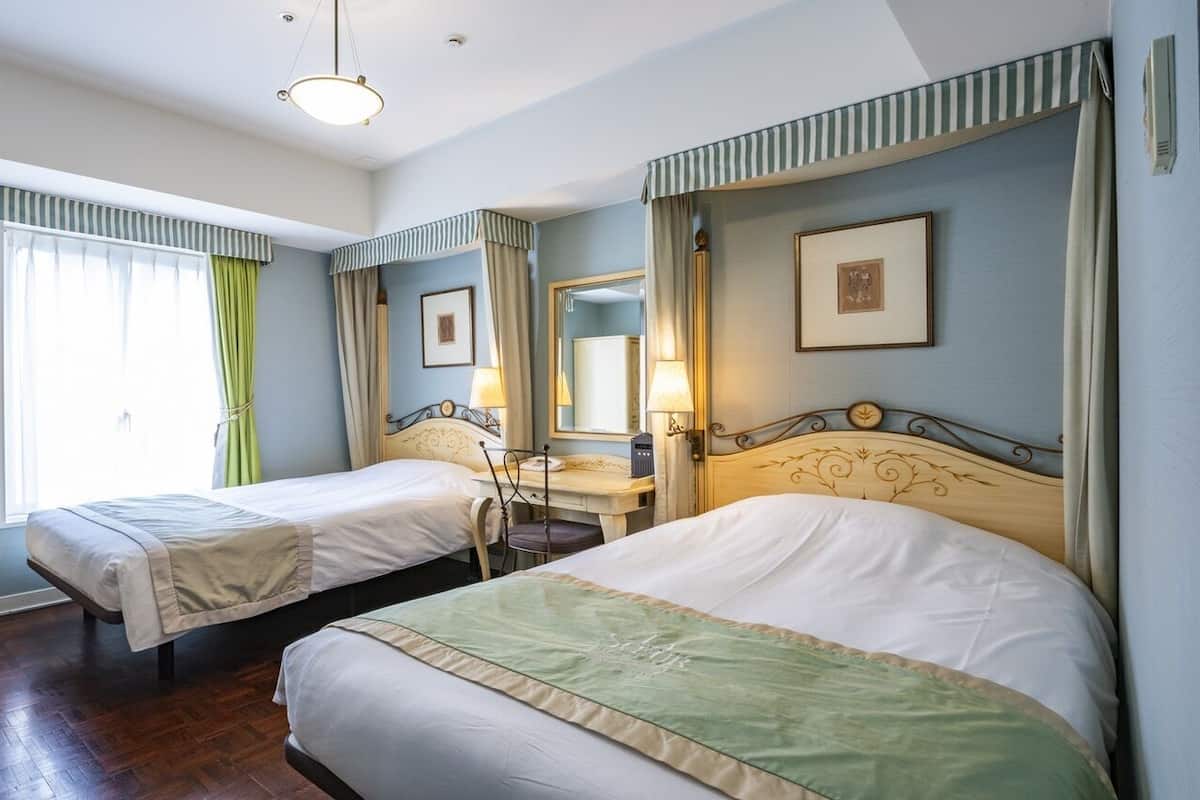 Habitación de hotel con dos camas, un escritorio, una silla, un armario y una ventana con cortinas.