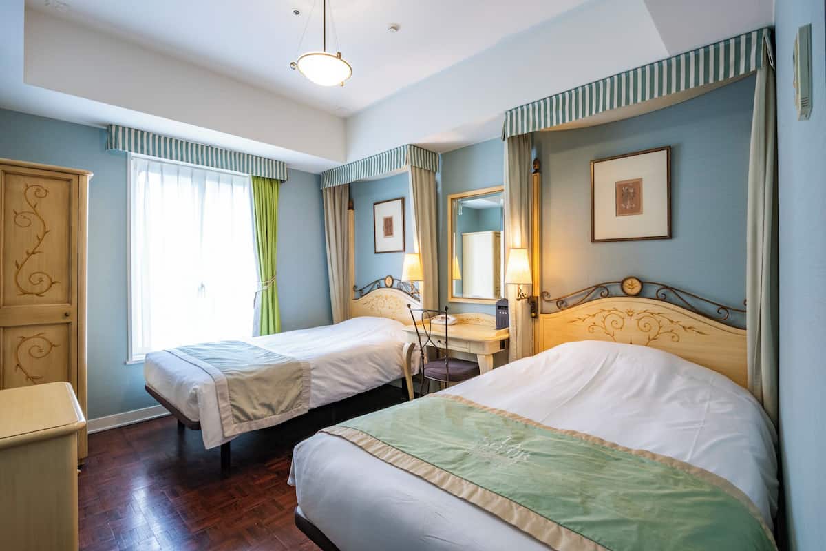Habitación de hotel con dos camas, un escritorio, una silla, un armario y una ventana con cortinas.