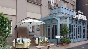 An outdoor dining area with tables and chairs, a covered seating area, and a building with a sign. - Hotel Monterey La Soeur Ginza (Tokyo)