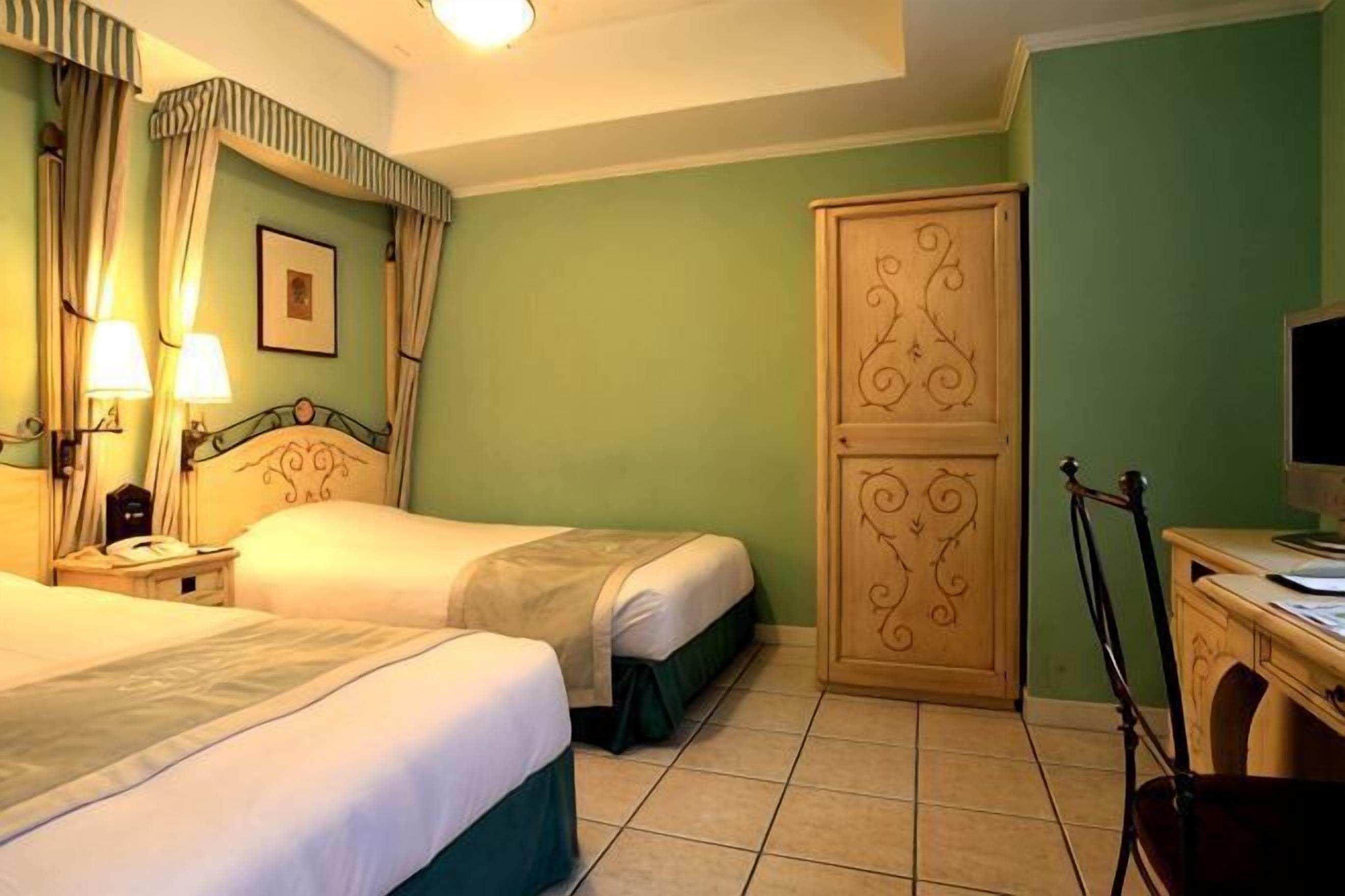 A hotel room with two beds, a wardrobe, a desk with a chair, and a television.