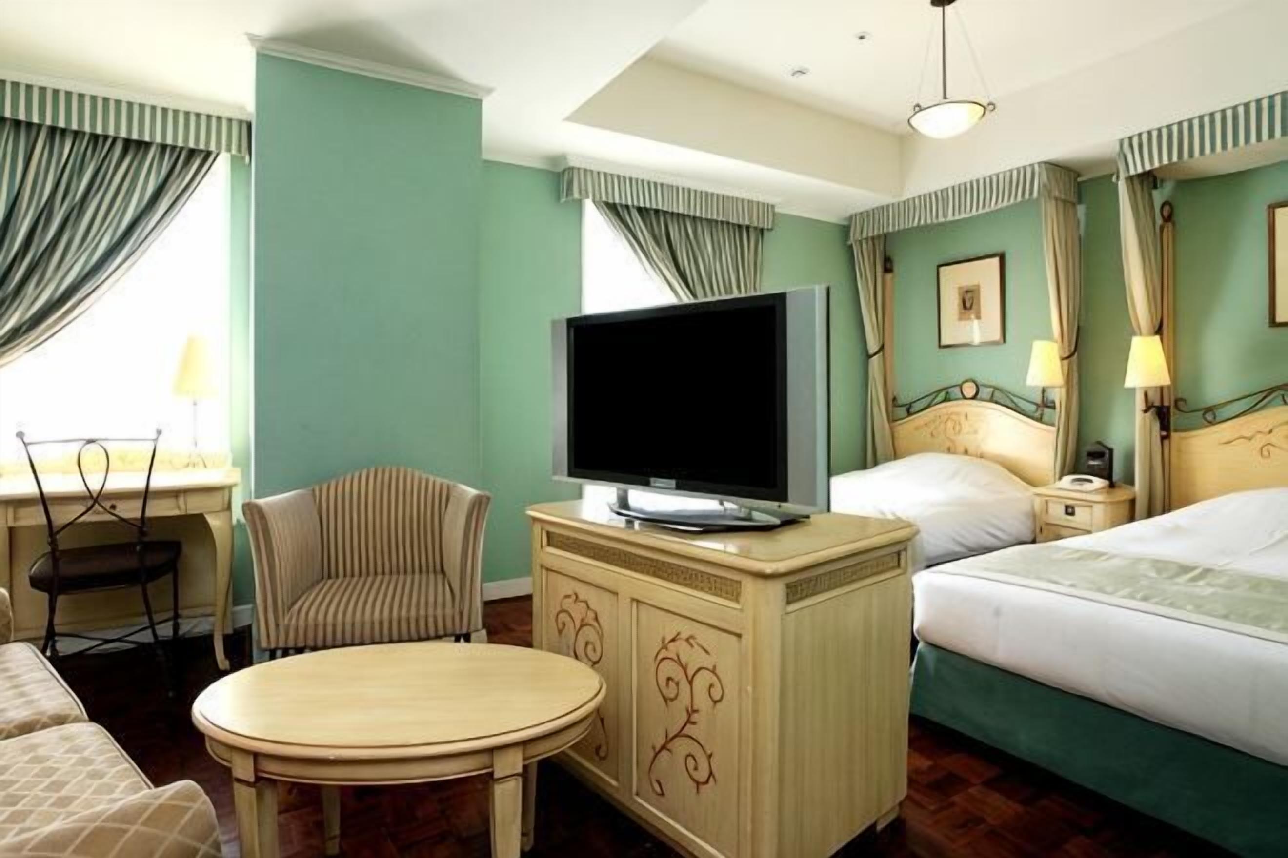 A hotel room with a bed, a TV on a cabinet, a chair, a table, and curtains.
