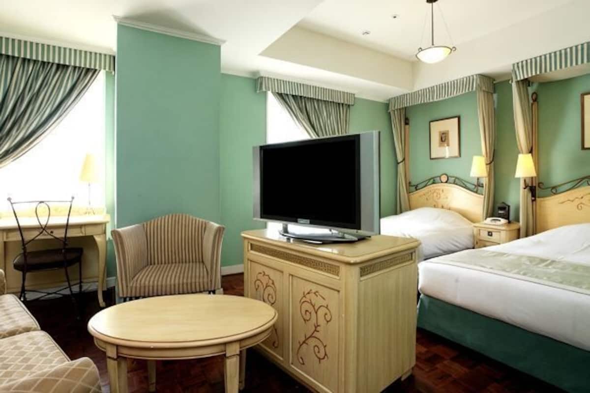 A hotel room with a bed, a TV on a cabinet, a chair, a table, and curtains.
