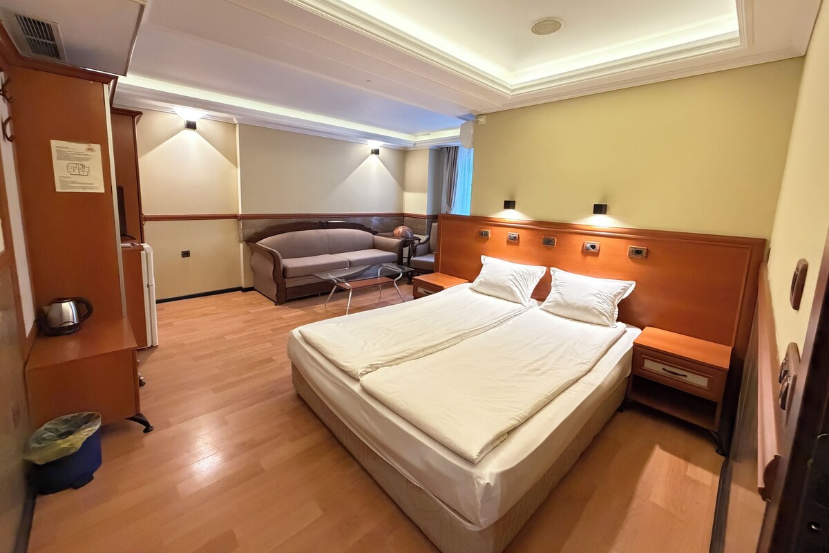 Une chambre d’hôtel avec un grand lit, une table de chevet en bois, un bureau avec une chaise, un canapé et une armoire.