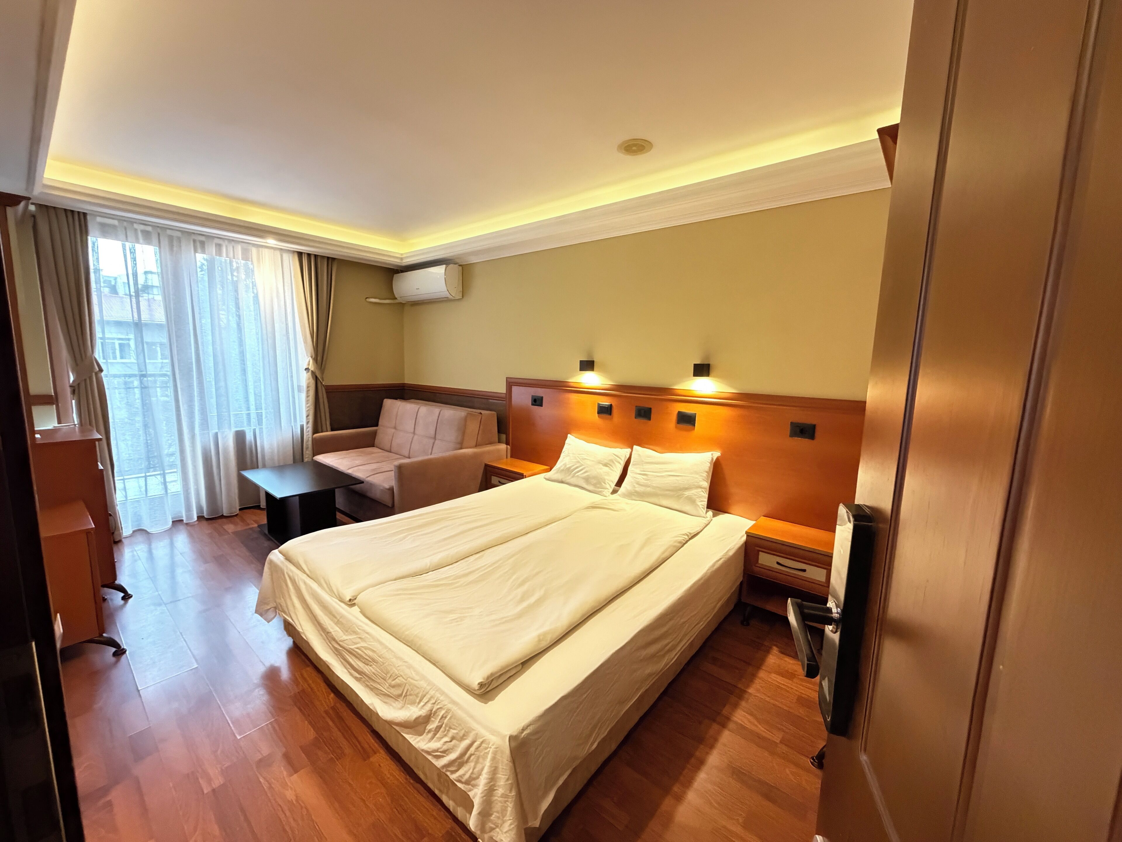 Una habitación de hotel con una cama grande, un sofá, un escritorio y una ventana con cortinas.