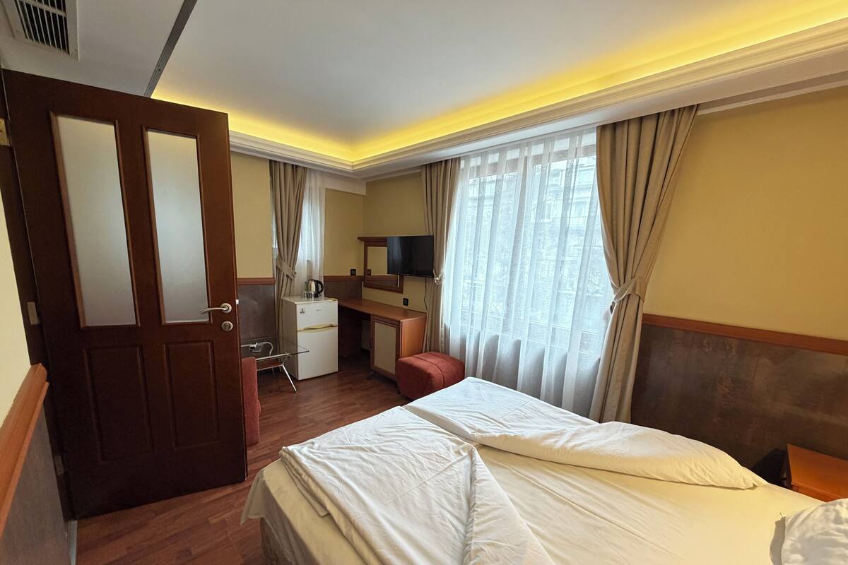 A hotel room with a bed, a desk, a chair, a television, and a window with curtains.