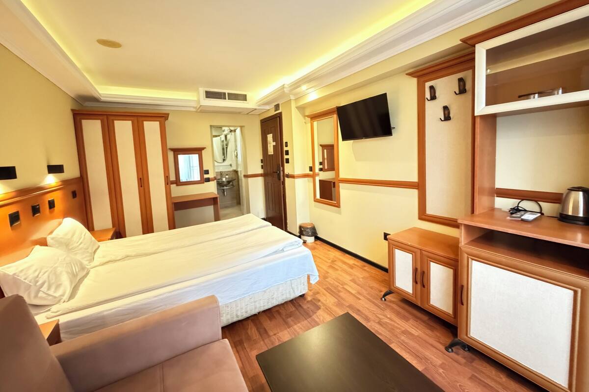 A hotel room with a double bed, a small sofa, a desk, a mirror, a television, and a wardrobe.