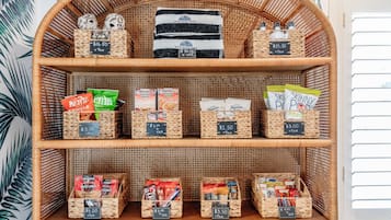 Una estantería de mimbre exhibe diversos productos empaquetados, como aperitivos y artículos de tocador, cada uno con su etiqueta de precio.