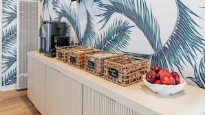 A counter with wicker crates labeled "Granola Bars," a coffee machine, and a bowl of apples. - Santa Monica Hotel (Santa Monica)