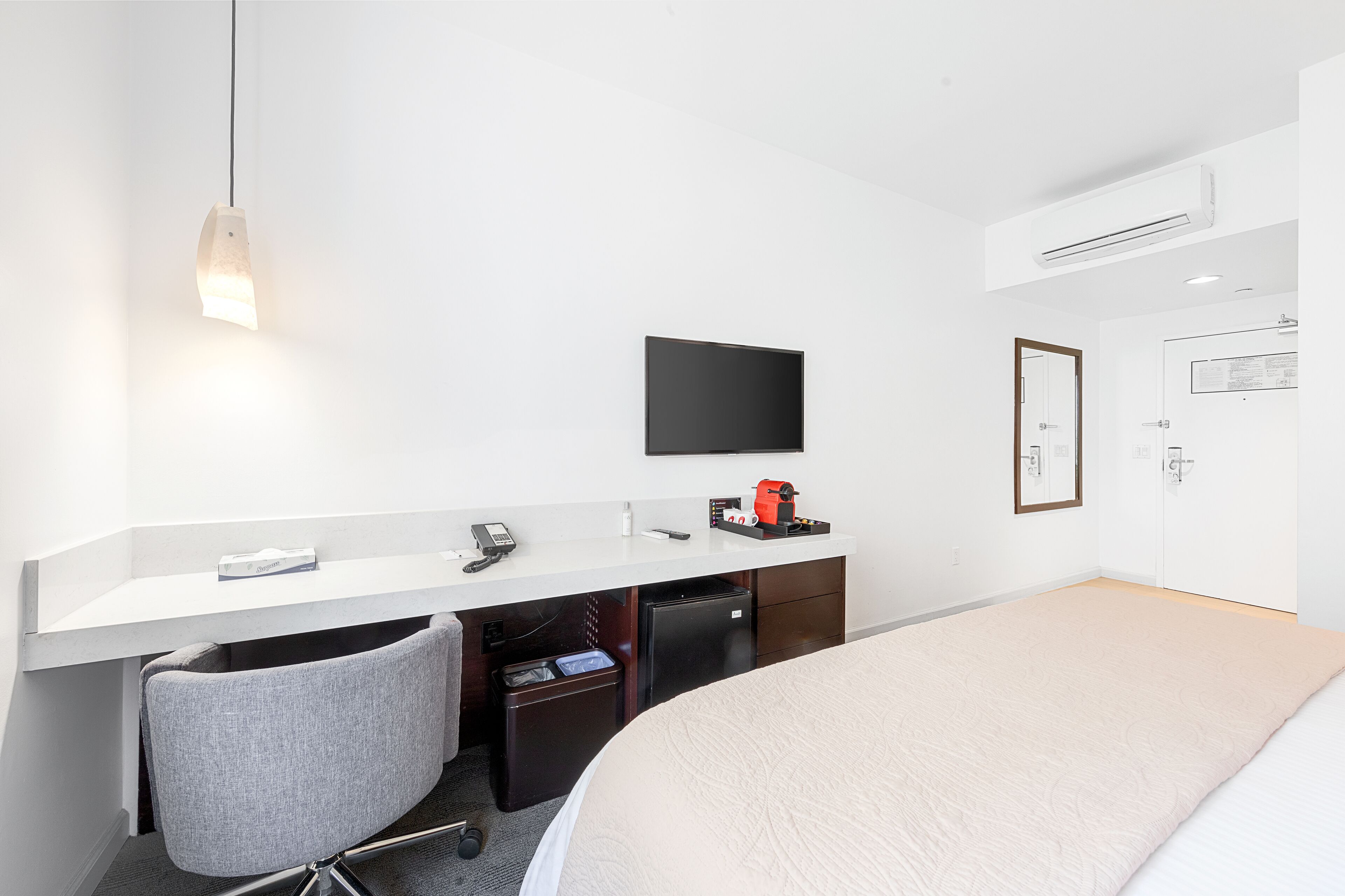 A hotel room with a bed, a desk with a chair, a television, and a small refrigerator.
