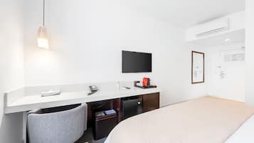 A hotel room with a bed, a desk with a chair, a television, and a small refrigerator.