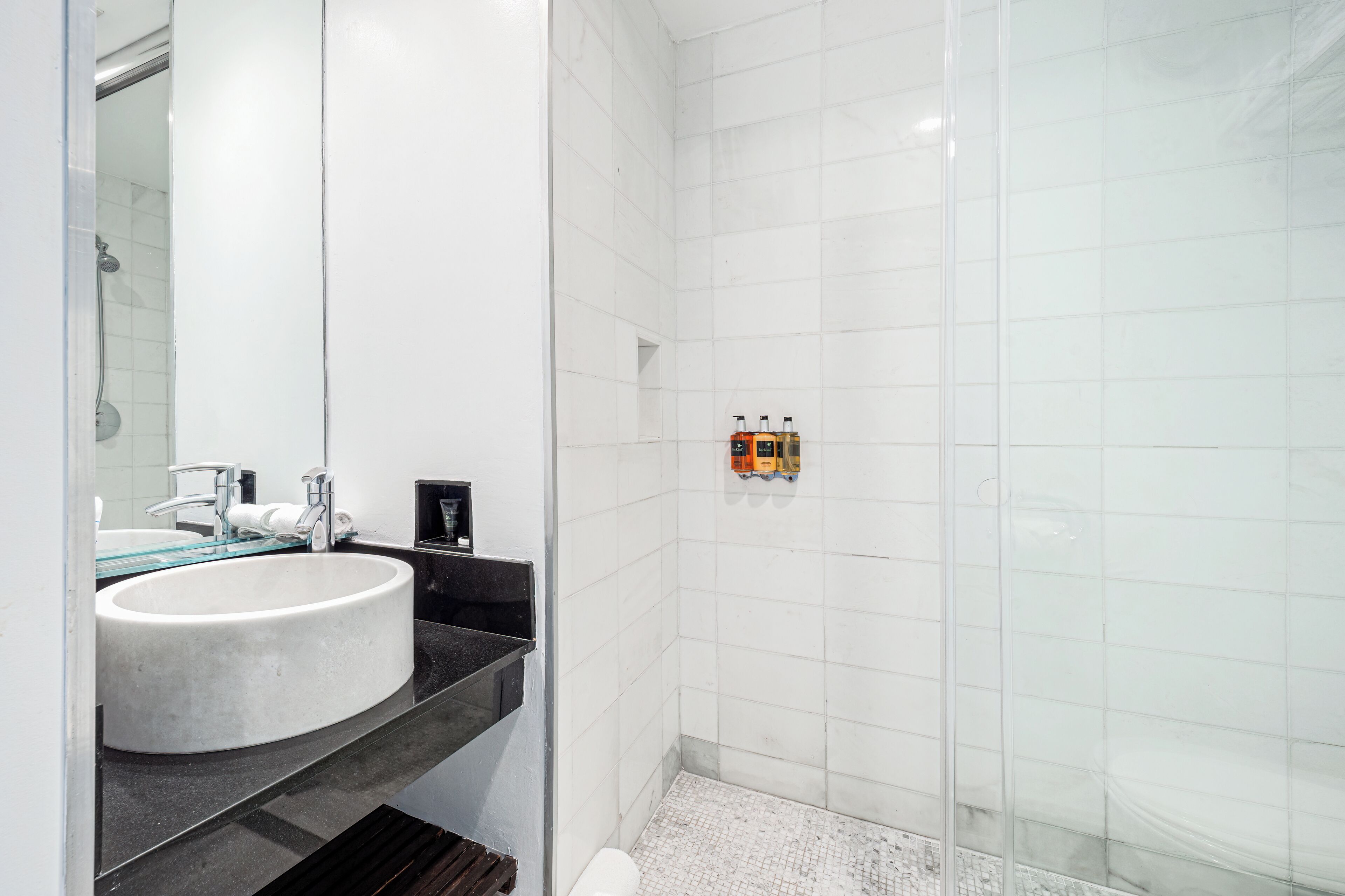 A modern bathroom with a white sink, black countertop, and a glass shower enclosure.