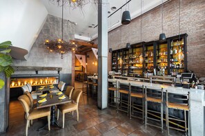 Un área de bar moderna con pared de ladrillo, luces colgantes y una barra con taburetes.