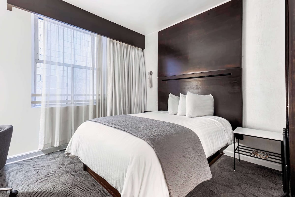 Una camera d'albergo moderna con un letto grande, un comodino, una sedia e una finestra con tende.