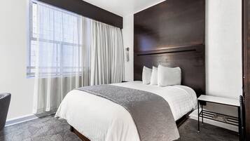 A modern hotel room with a large bed, a bedside table, a chair, and a window with curtains.