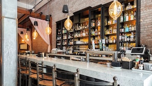 A bar with a marble countertop, hanging pendant lights, and a brick wall. - The O Hotel, Trademark Collection by Wyndham (Los Angeles)