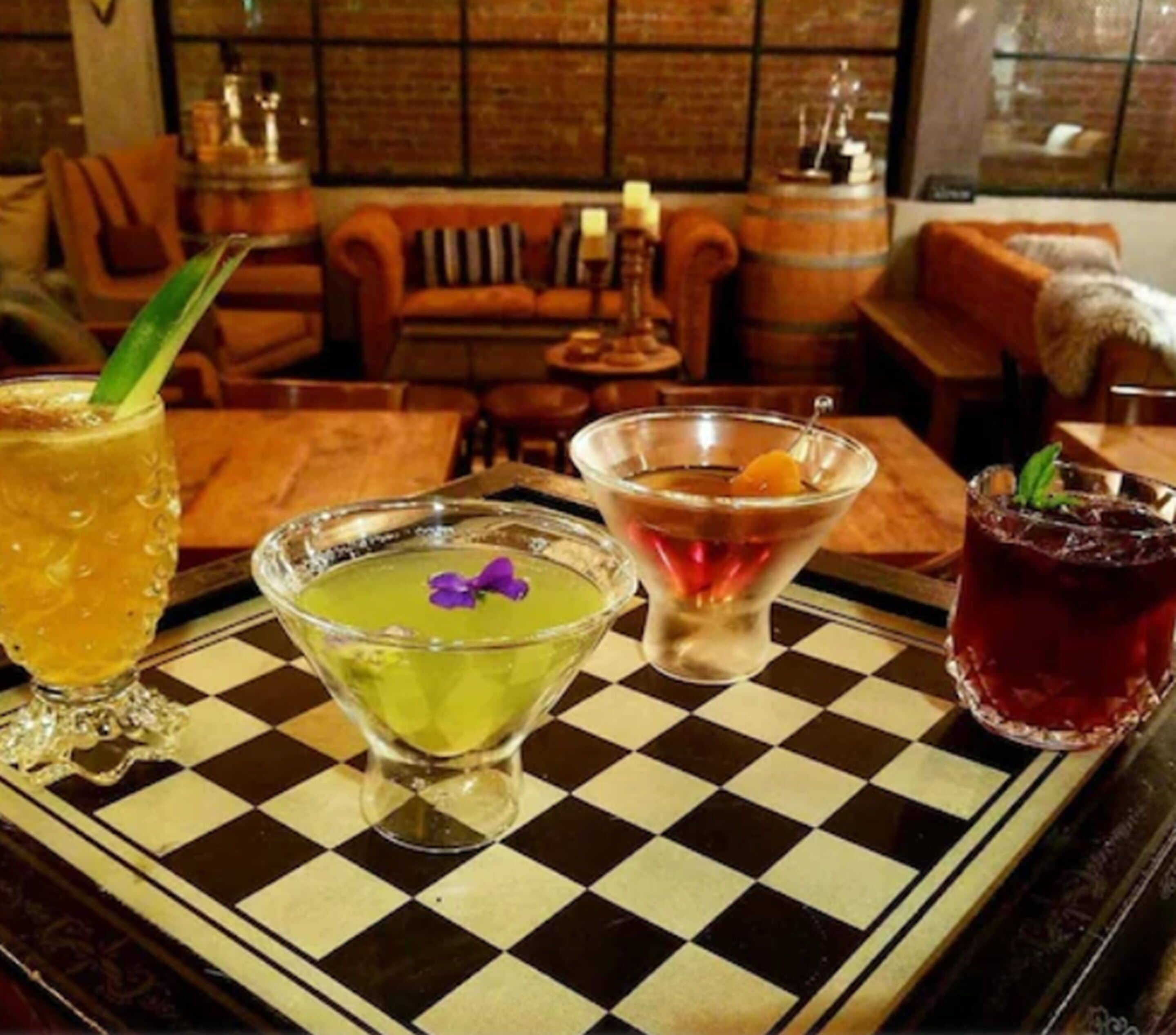 Un espace bar avec un sol à carreaux, une variété de boissons servies dans différents types de verres, et un mur de briques en arrière-plan.