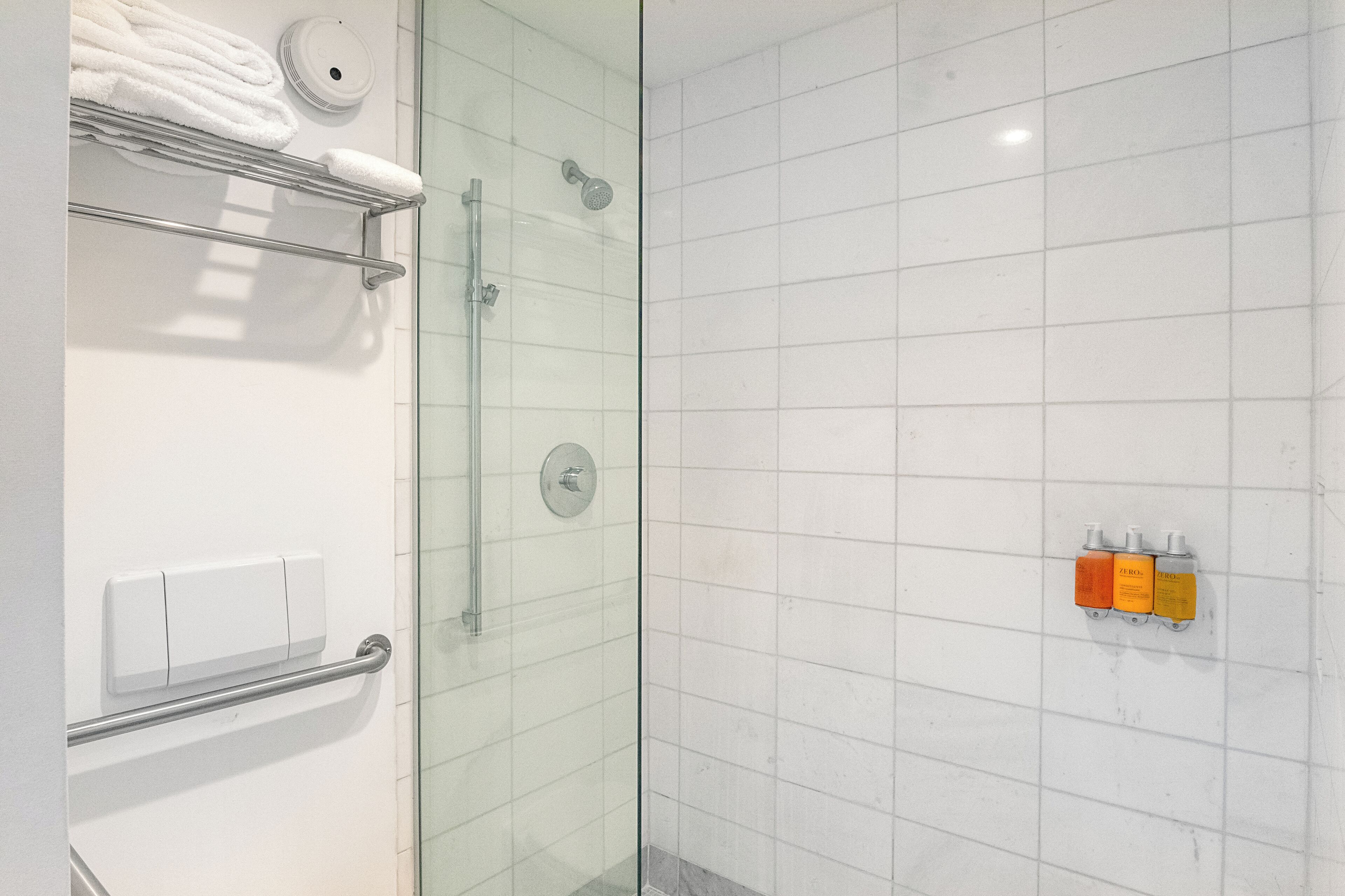 Um banheiro moderno com box de vidro, porta-toalhas com toalhas dobradas e um dispensador de sabonete fixado na parede.