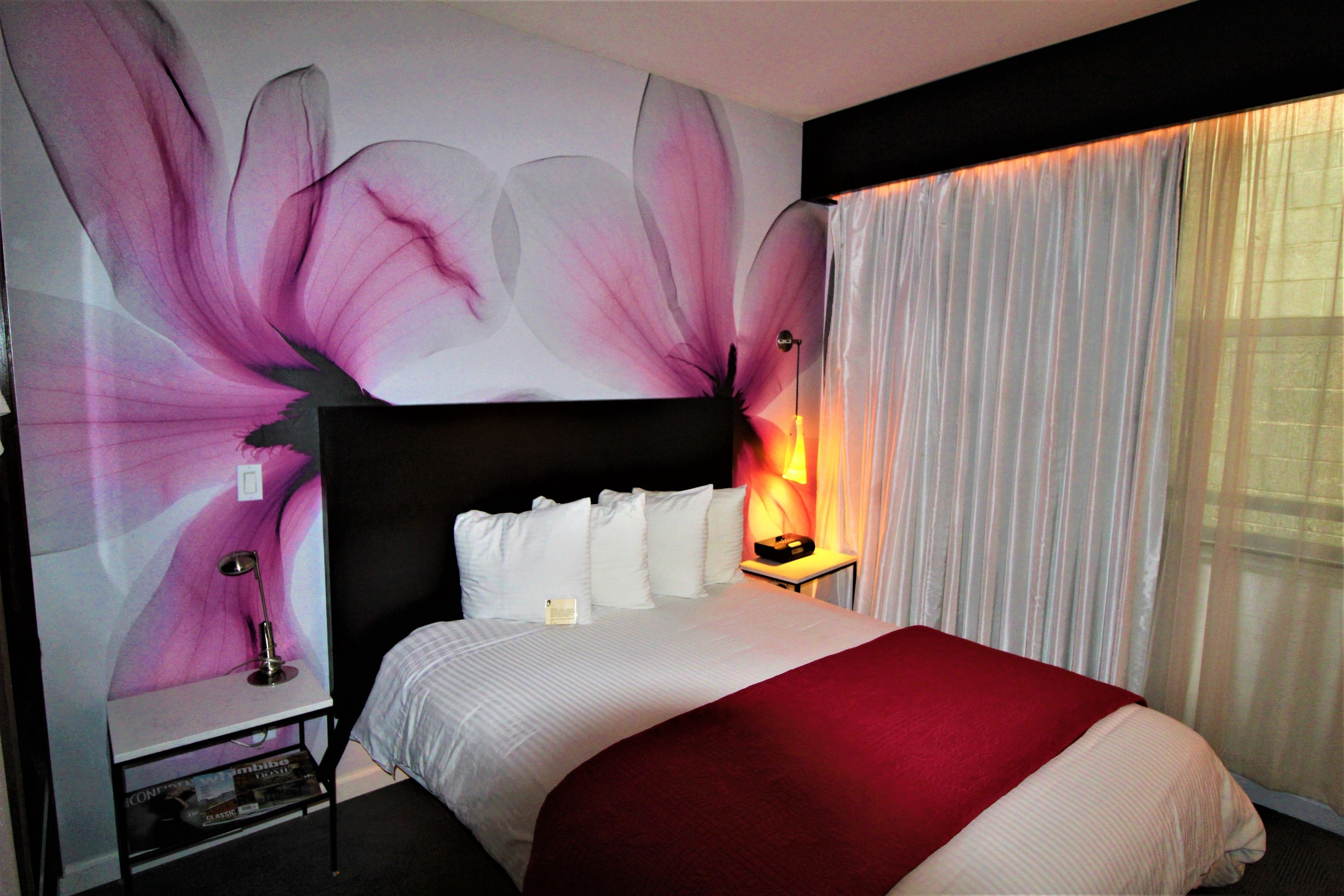 A hotel room with a large bed, a nightstand with a lamp, and a wall with a floral design.