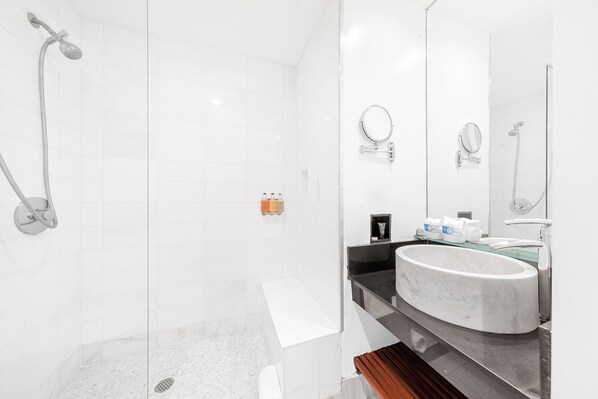 Un baño moderno con ducha de vidrio, lavamanos de mármol y un espejo grande.