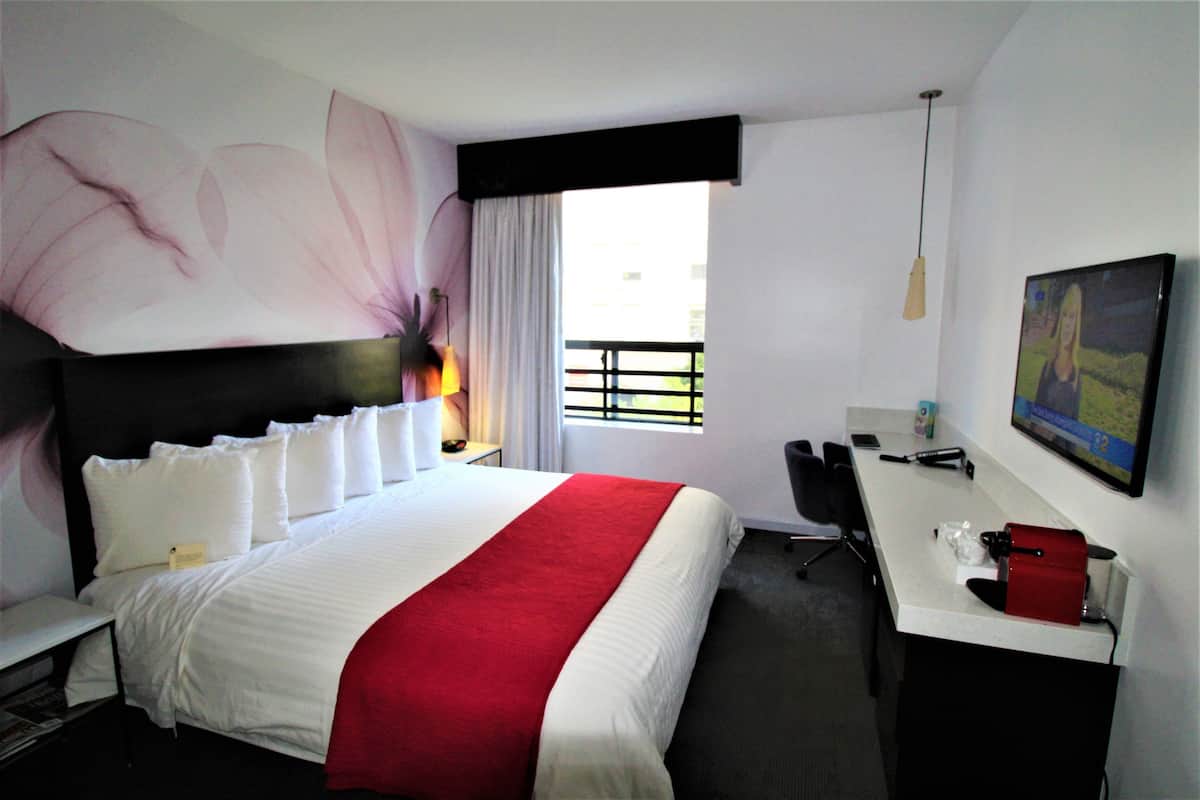 Camera d'albergo con un letto grande, una scrivania, una sedia, una televisione e una finestra con tende.