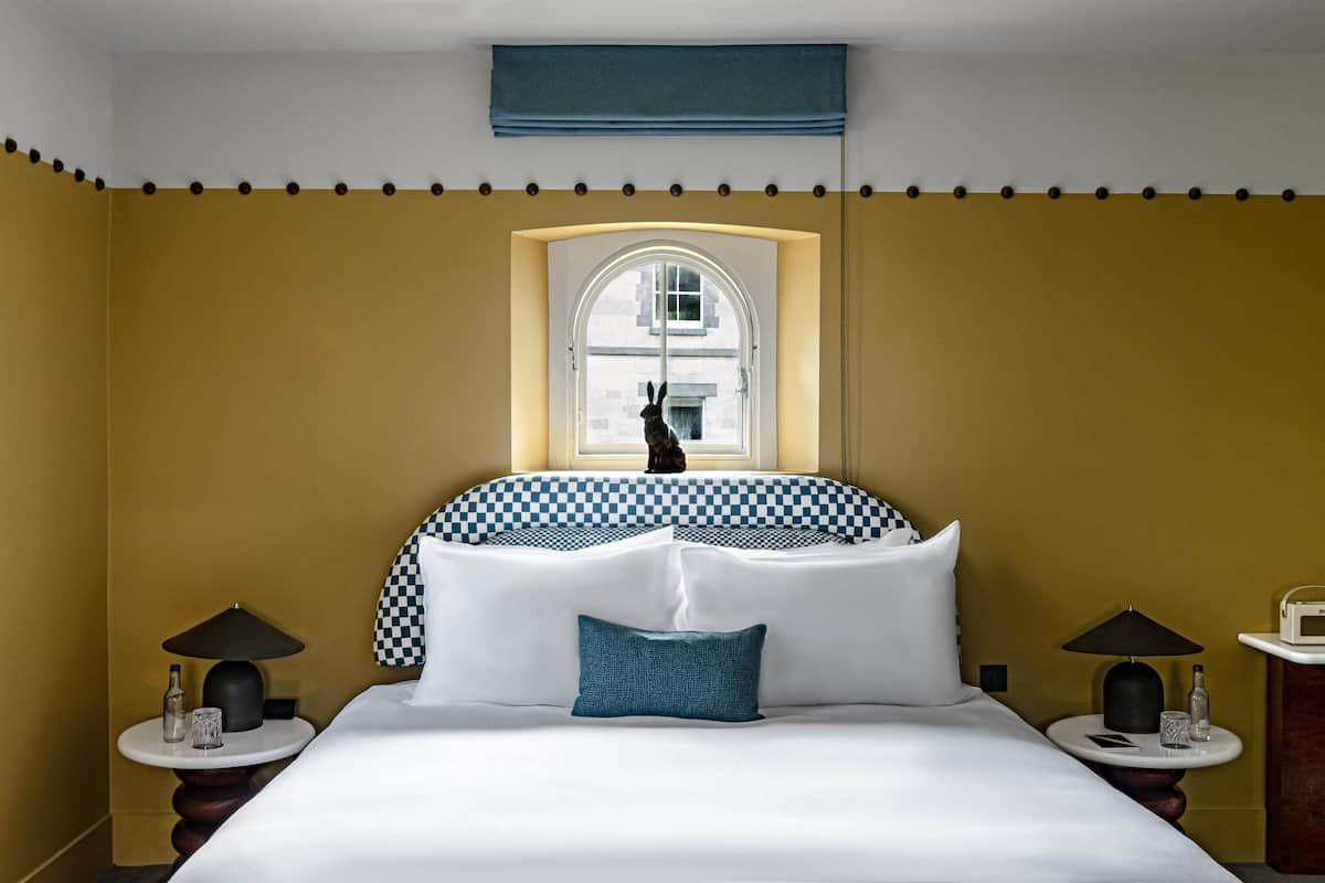 A hotel room with a large bed, checkered headboard, a window with a view, and two bedside tables with lamps.