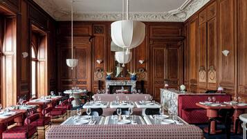 A formal dining room with wooden paneling, marble tables, and red upholstered chairs.