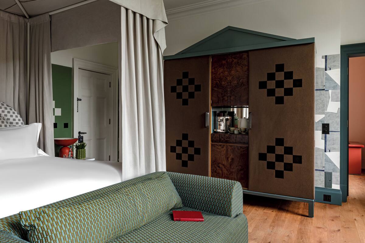 A hotel room with a bed, a green sofa, a red book, a wardrobe with a checkered pattern, and a bathroom visible through an open door.