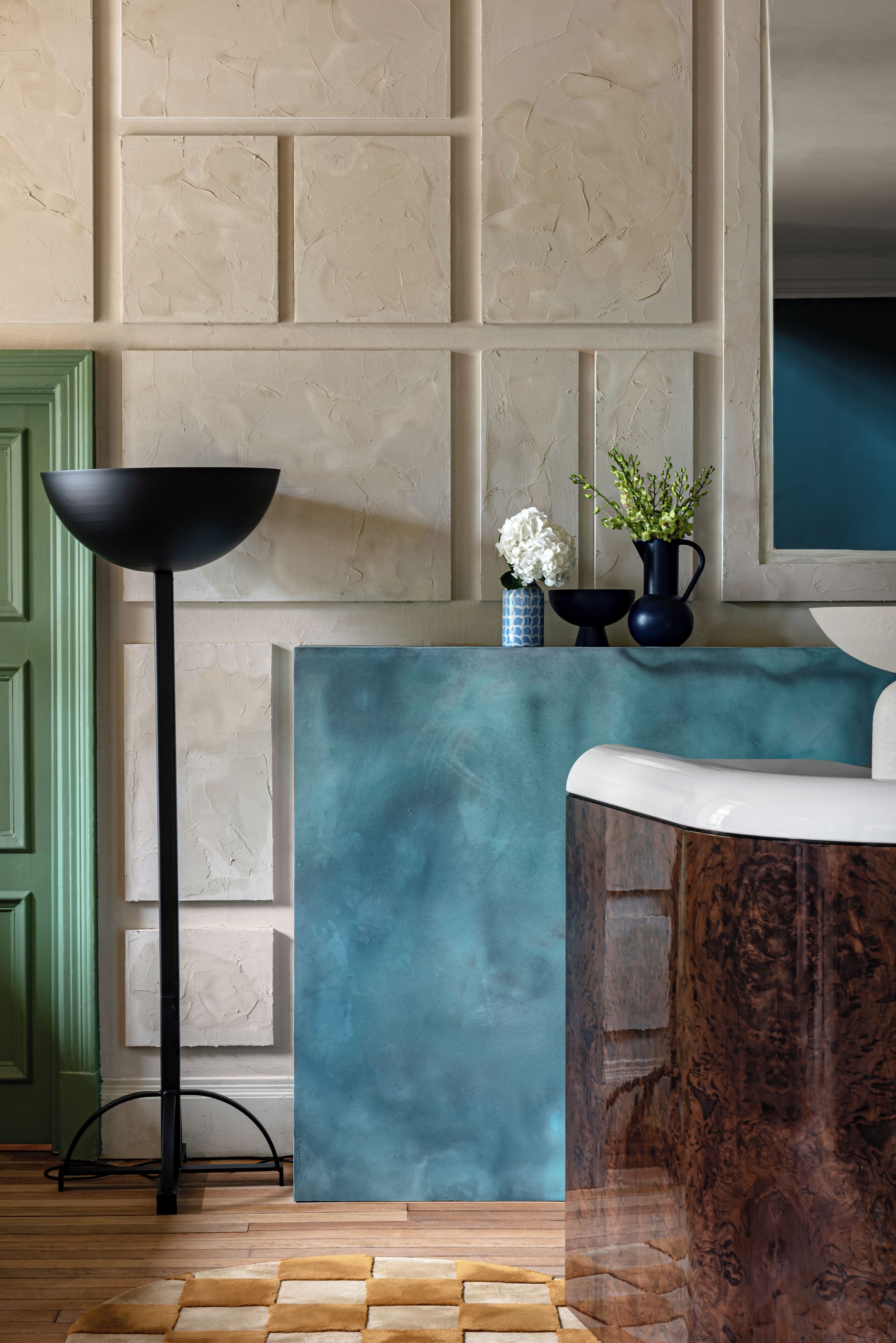 A reception area with a teal-colored counter, a black floor lamp, and a wooden side table.