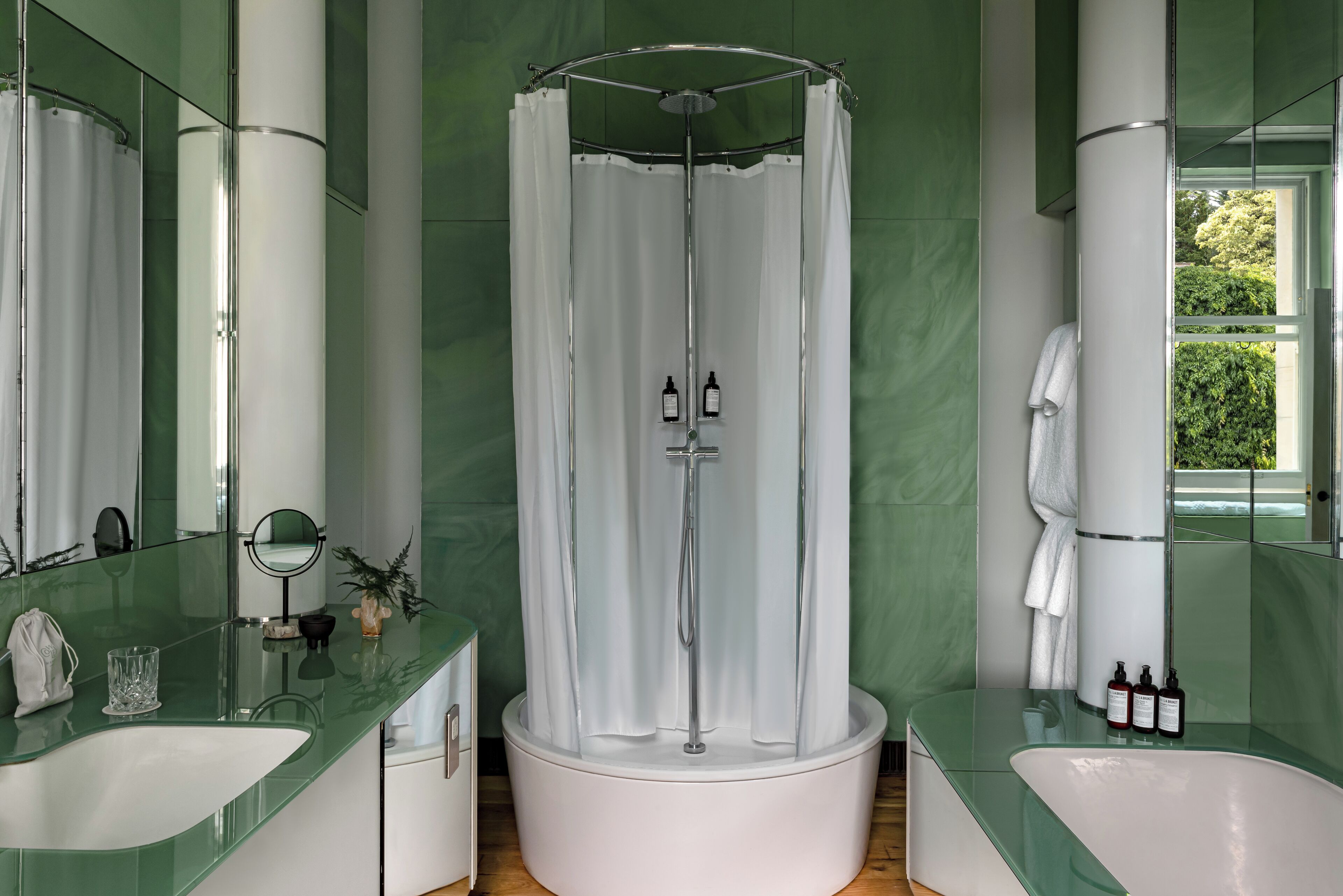 A modern bathroom with a glass shower enclosure, a white bathtub, and a green marble vanity.