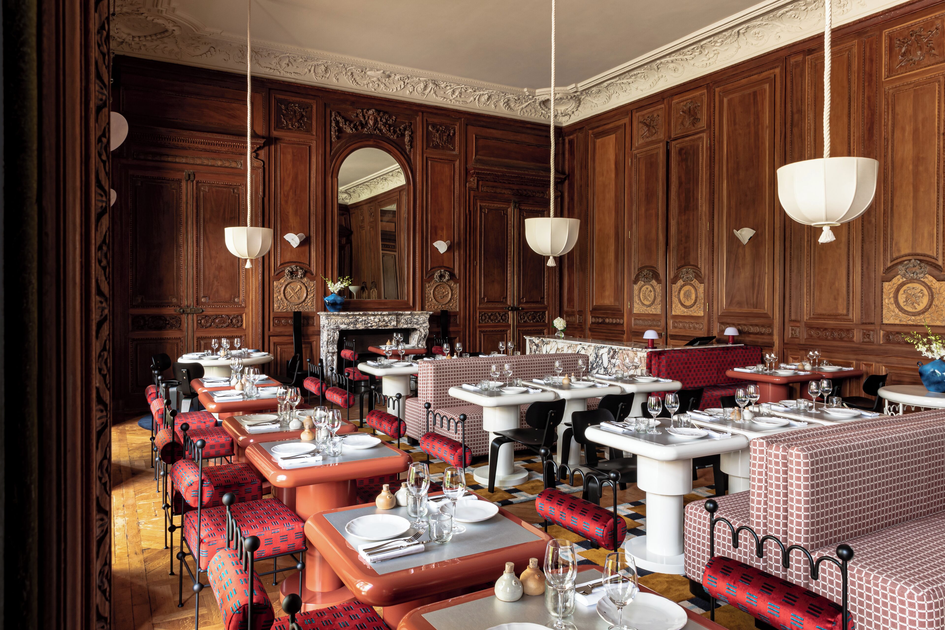 Une salle à manger élégante, dotée de plusieurs tables et chaises, de boiseries et de décorations ornementales au plafond.