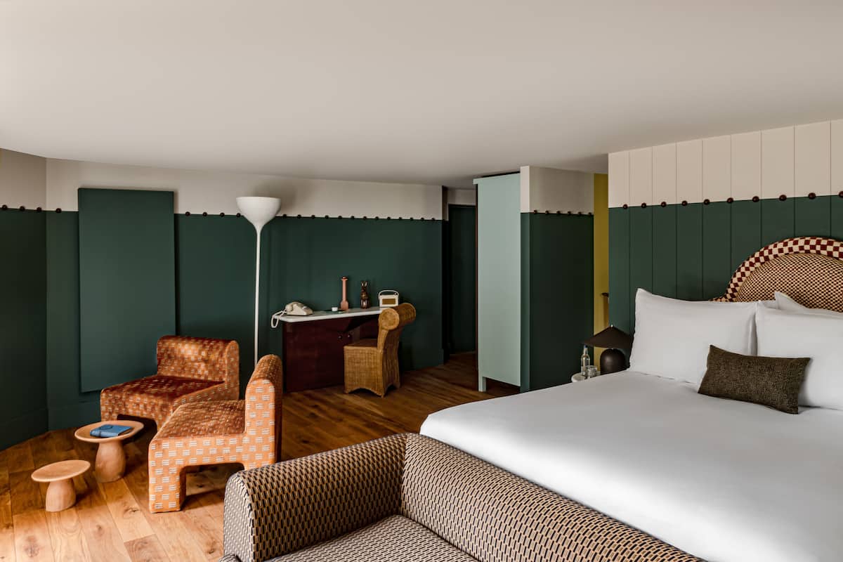 A hotel room with a large bed, two armchairs, a small desk, and a lamp.