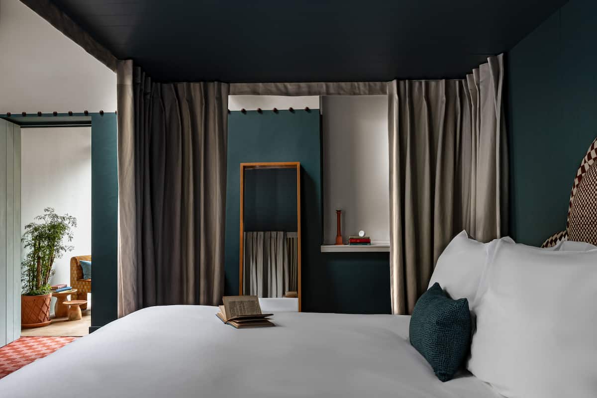 A bedroom with a large bed, a bedside table, a mirror, and a view of a balcony.