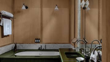 A bathroom with a green vanity, a large bathtub, two sinks, and a mirror. There are towels on a rack and a bottle of shampoo on the counter.