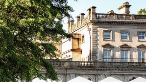 A large building with a formal entrance, a well-maintained garden, and outdoor seating areas with umbrellas. - Cowley Manor Experimental (Cheltenham)