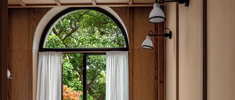 A bathroom with a wooden vanity, a white sink, and a view of a balcony with potted plants.