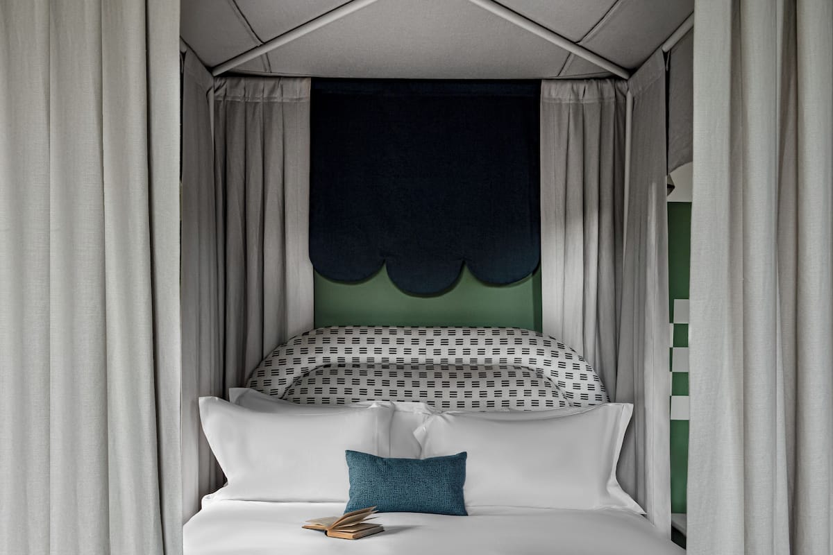 A bedroom with a canopy bed, white bedding, a teal pillow, and a green wall.