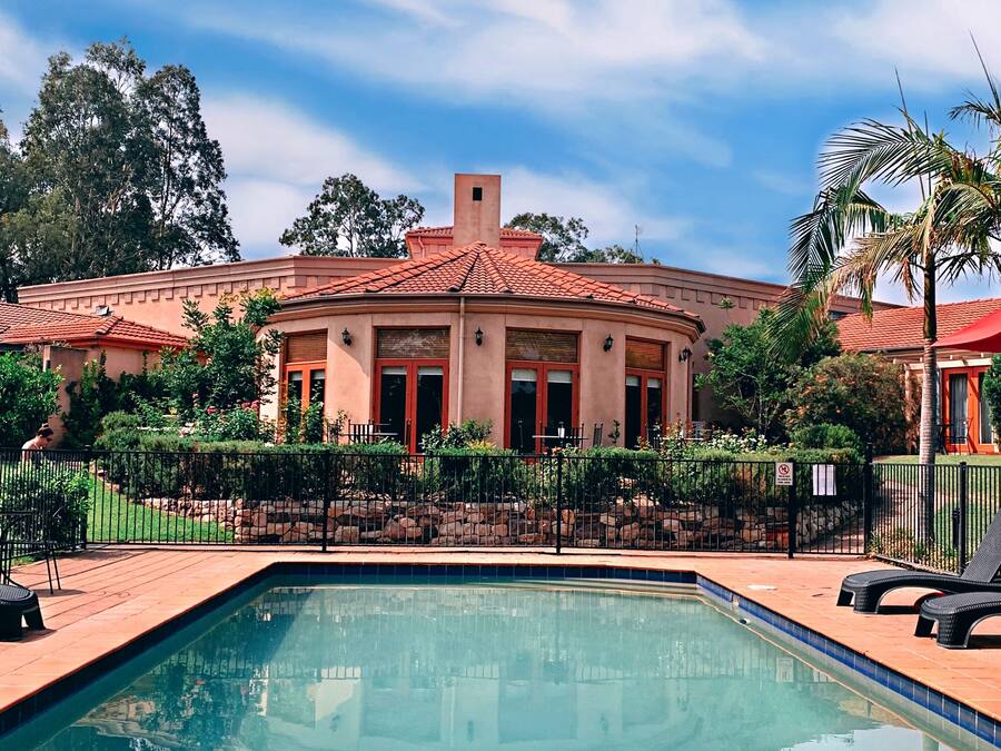A pool area with a building in the background, surrounded by a fence and palm trees.