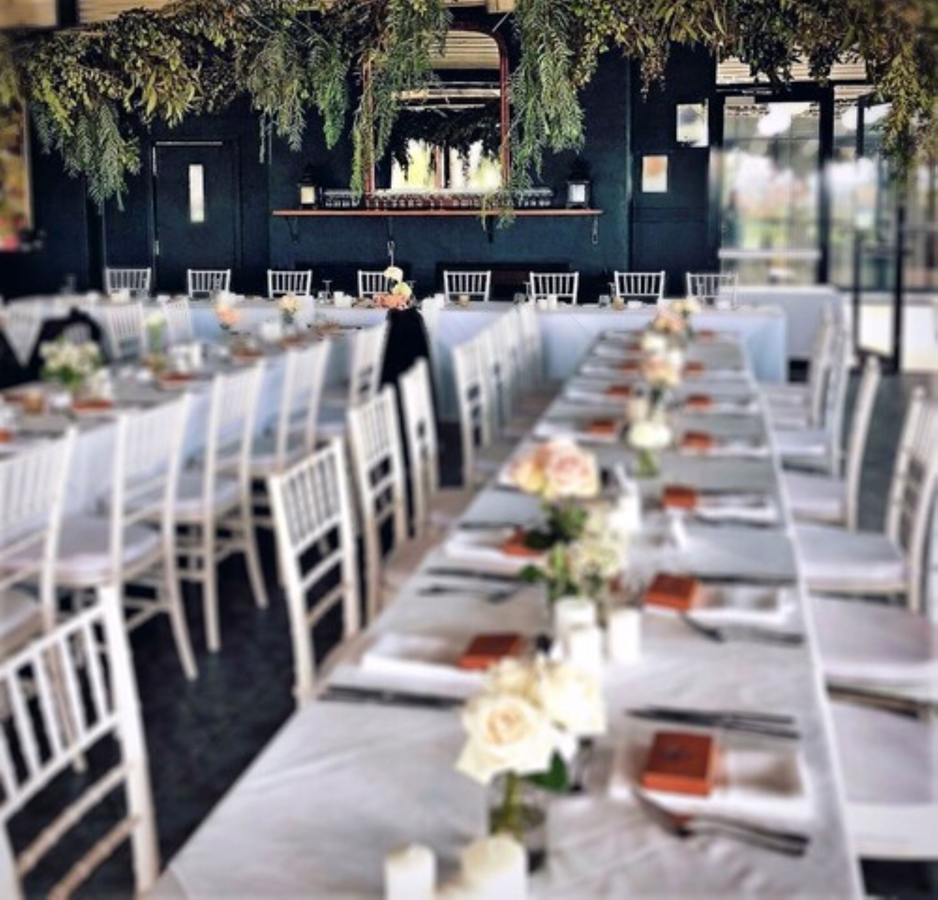 A long banquet table with white chairs, adorned with floral centerpieces and orange napkins.