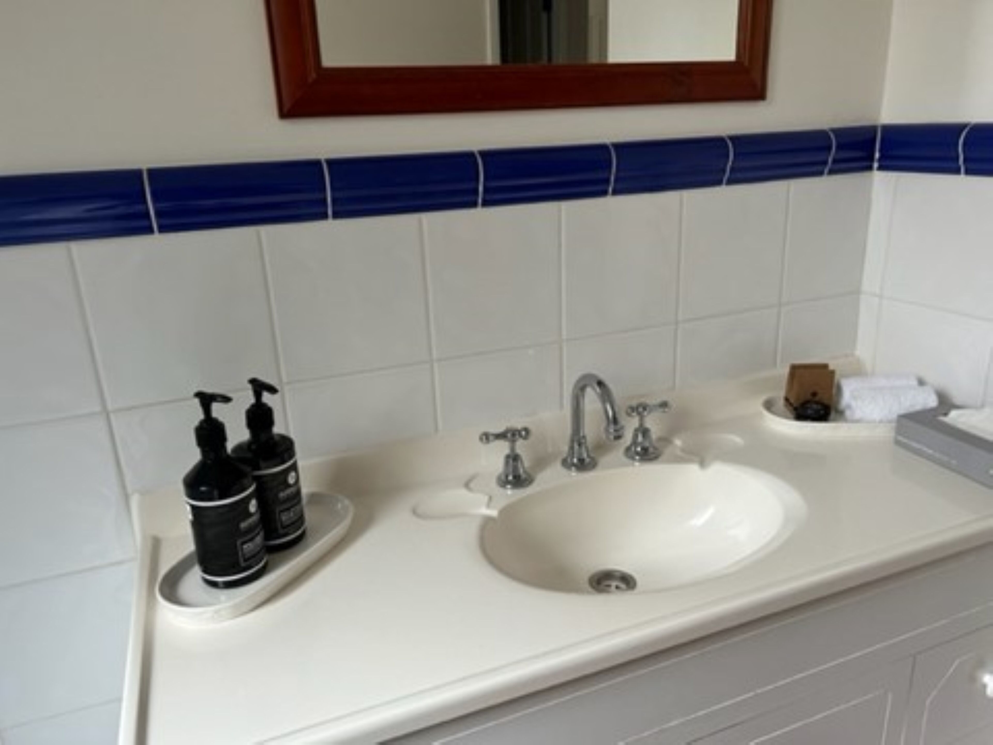 Un baño con un lavamanos blanco, dos dispensadores de jabón negros, un espejo sobre el lavamanos y un salpicadero de azulejos azul y blanco.
