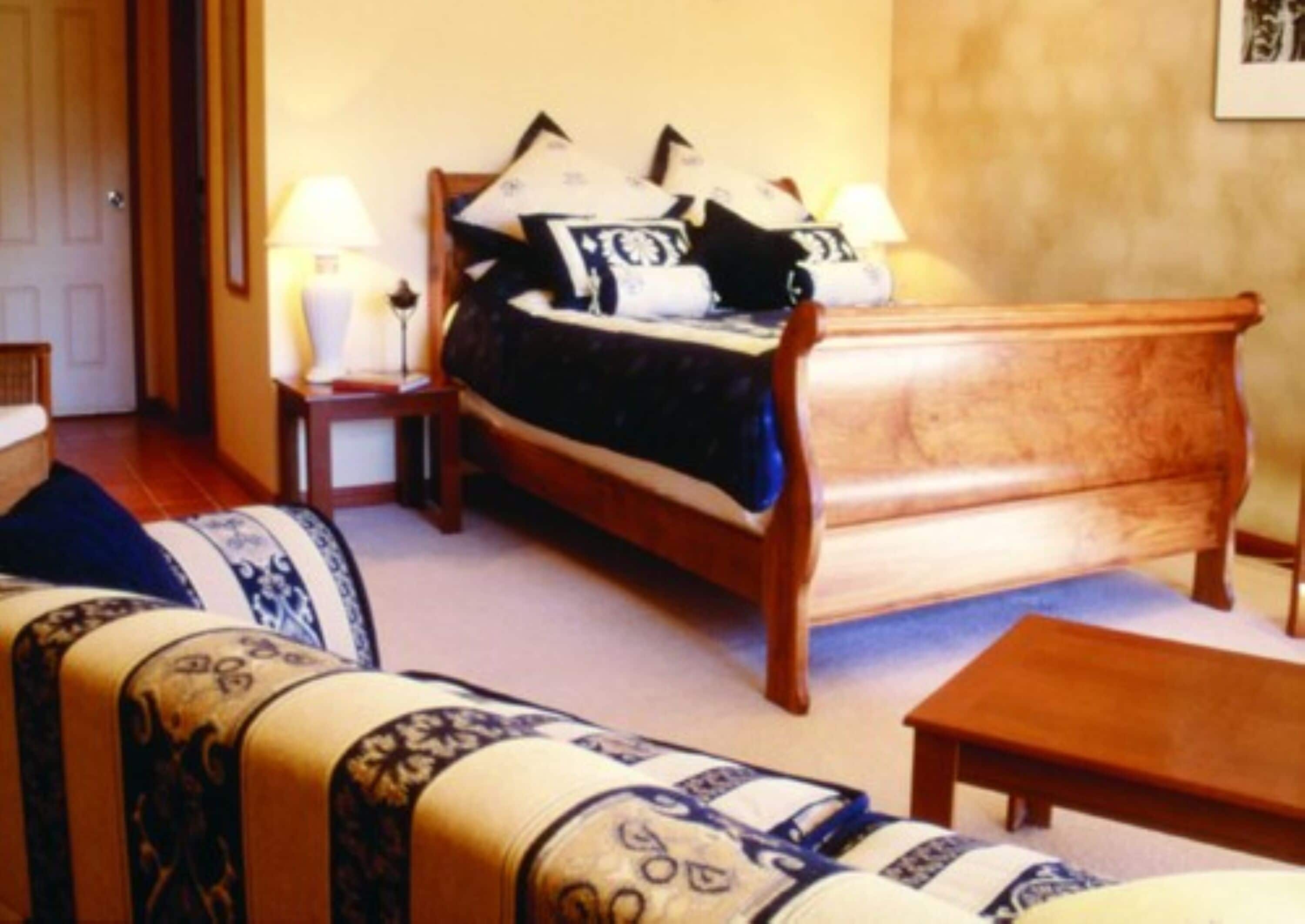 Un dormitorio con una cama de madera, una mesita de noche, una lámpara, un sofá y una pequeña mesa de madera.