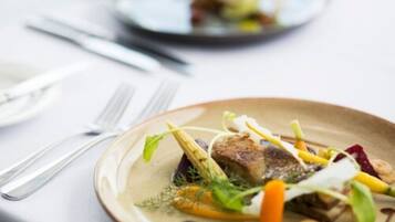 A plate of food with various vegetables and a piece of meat, accompanied by cutlery on a table.