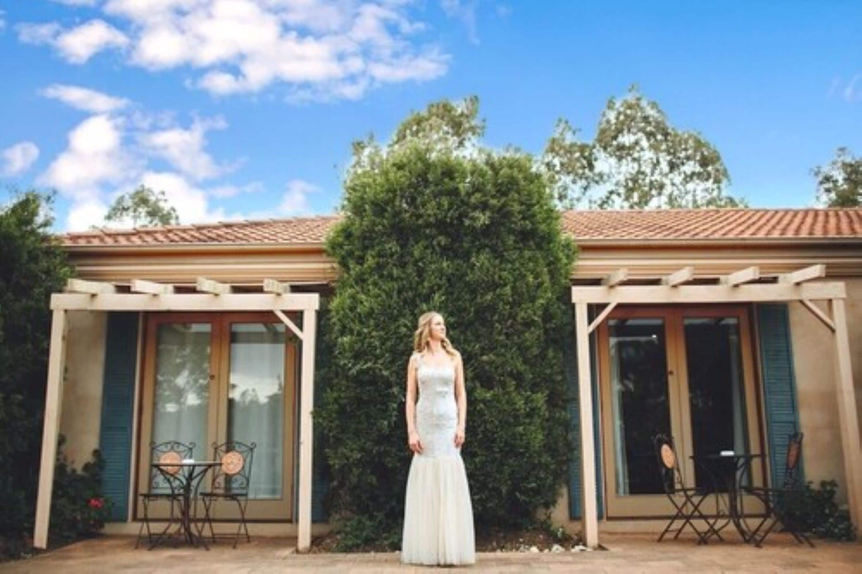 Una mujer con vestido blanco parada frente a un edificio con una pérgola y dos mesas.