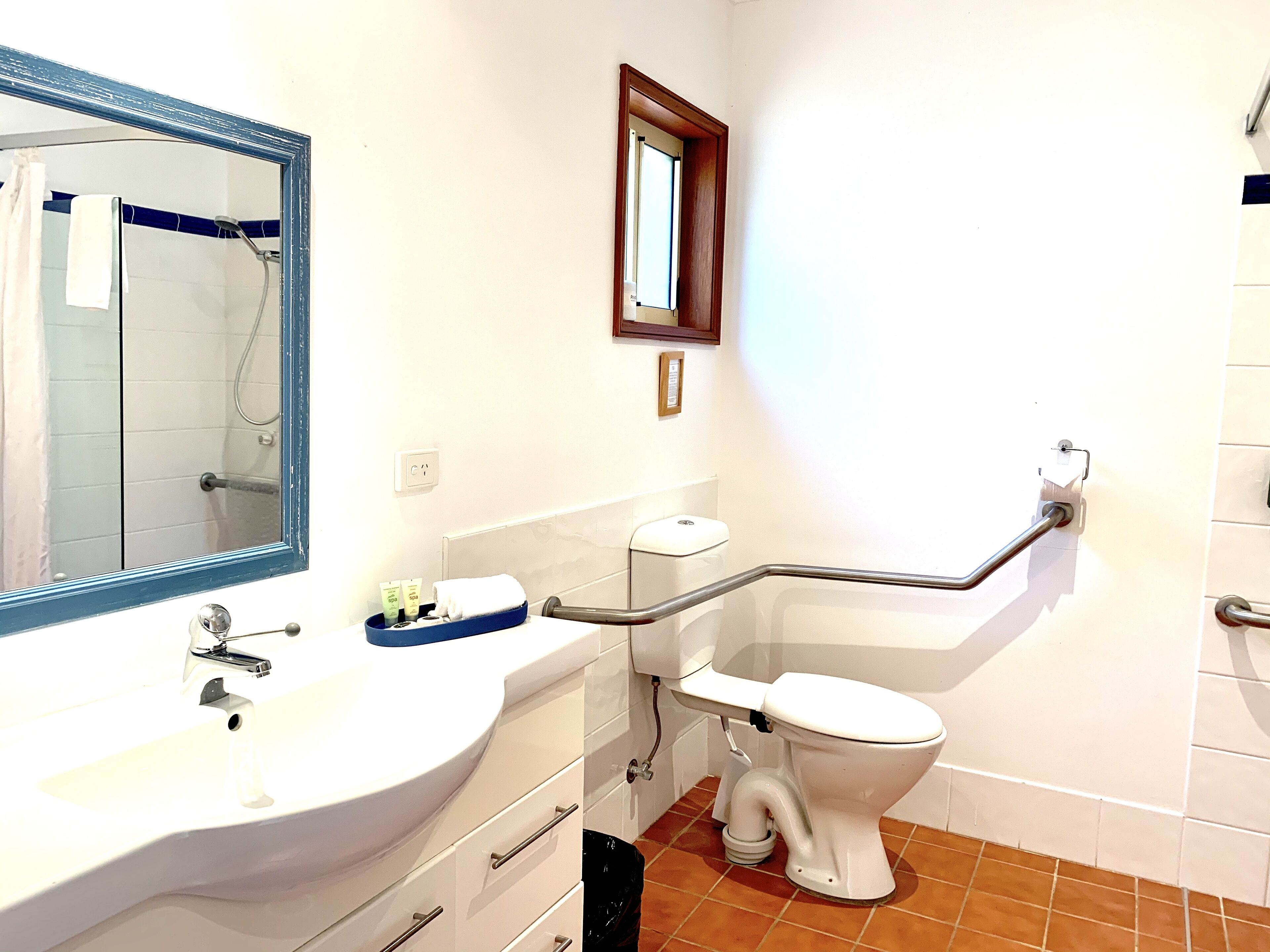 A bathroom with a white sink, a mirror, a shower, and a toilet with a grab bar.