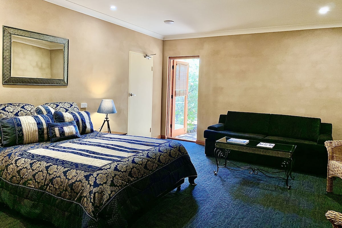 A bedroom with a large bed, a green sofa, a small table, and a door leading to a balcony.